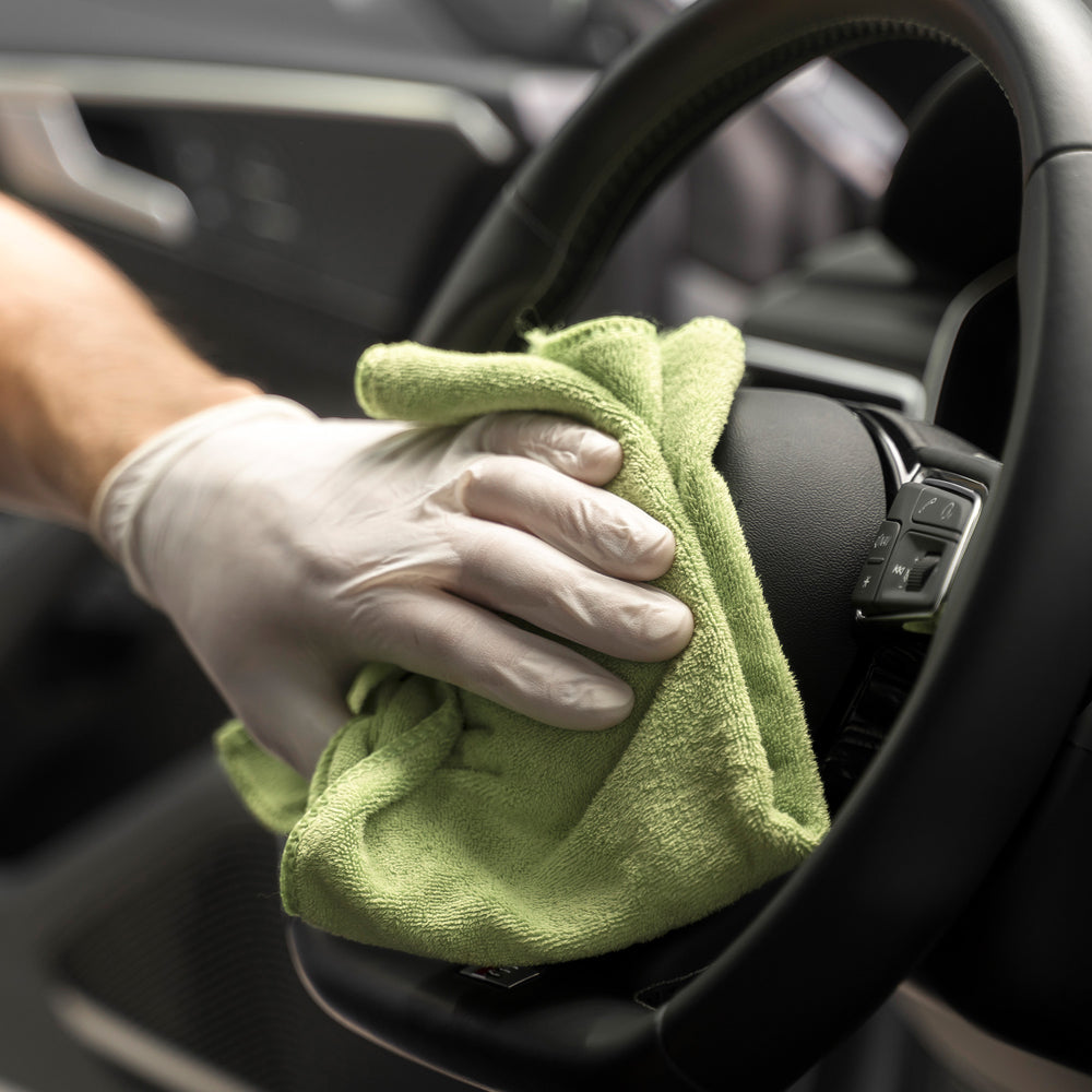 
                      
                        Cleaning car steering wheel with green microfiber cloth and glove.
                      
                    